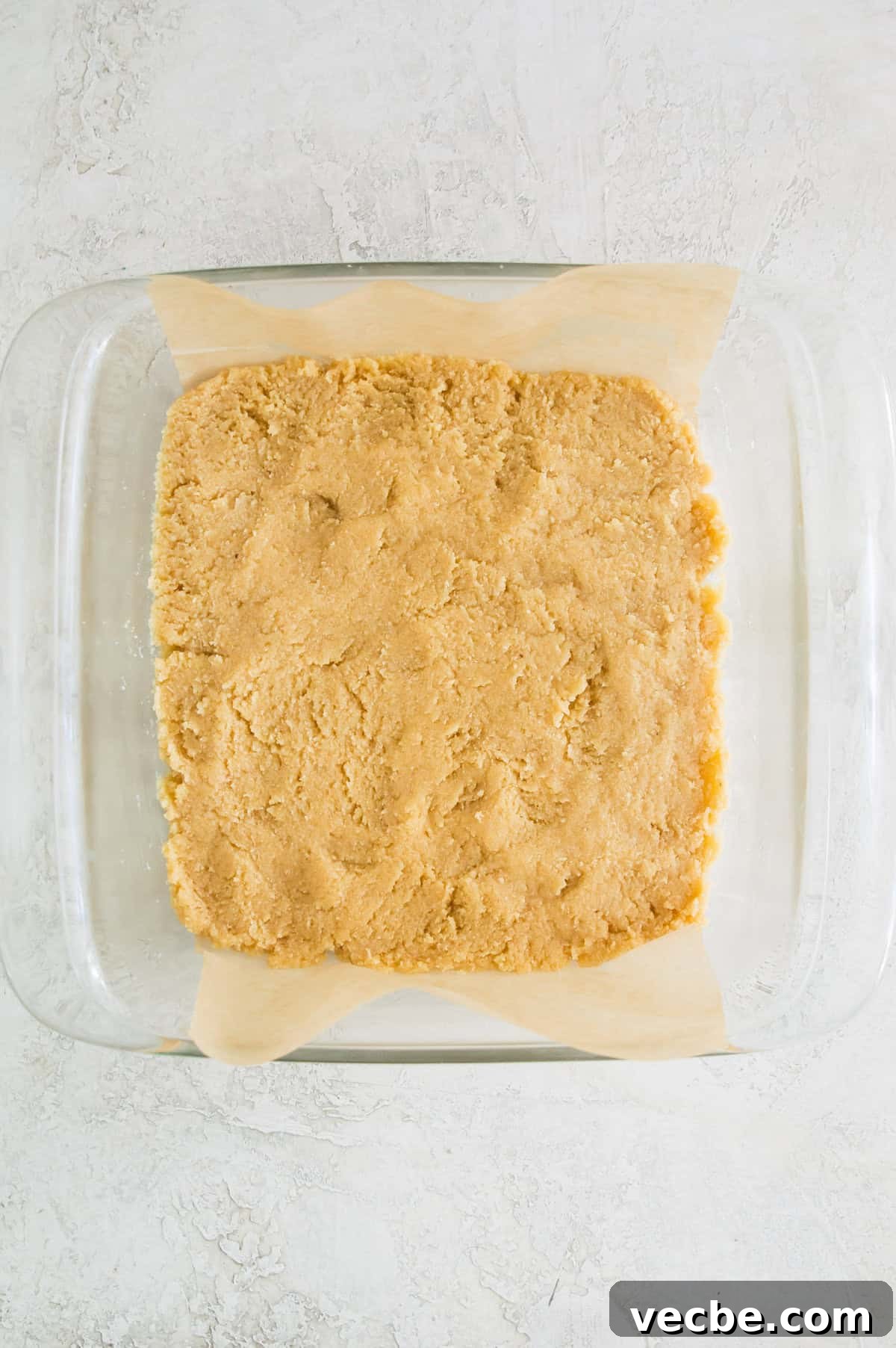 Apple Pie Bars Gluten Free Vegan and Paleo 5 A square baking pan lined with parchment paper with a shortbread dough in it.