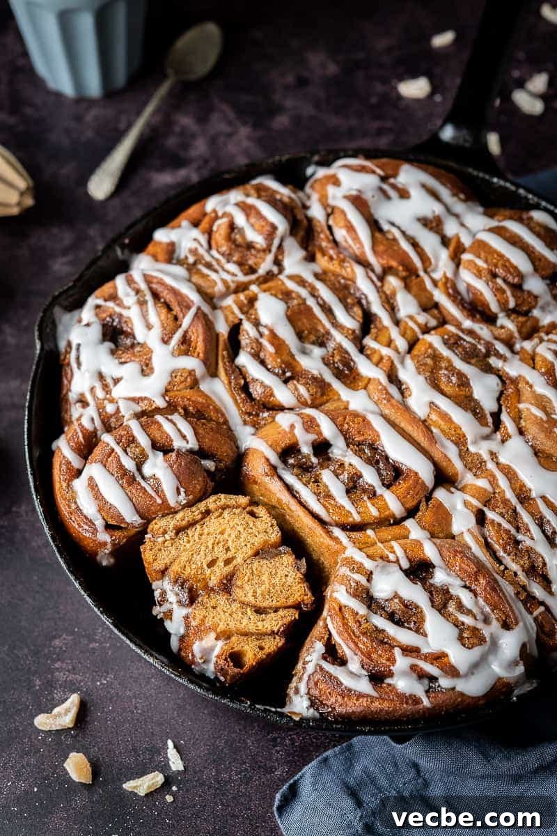 Vegan gingerbread cinnamon rolls with ginger, cinnamon, treacle and sweet glaze side shot of vegan gingerbread cinnamon rolls in a cast iron skillet, one sliced in half.