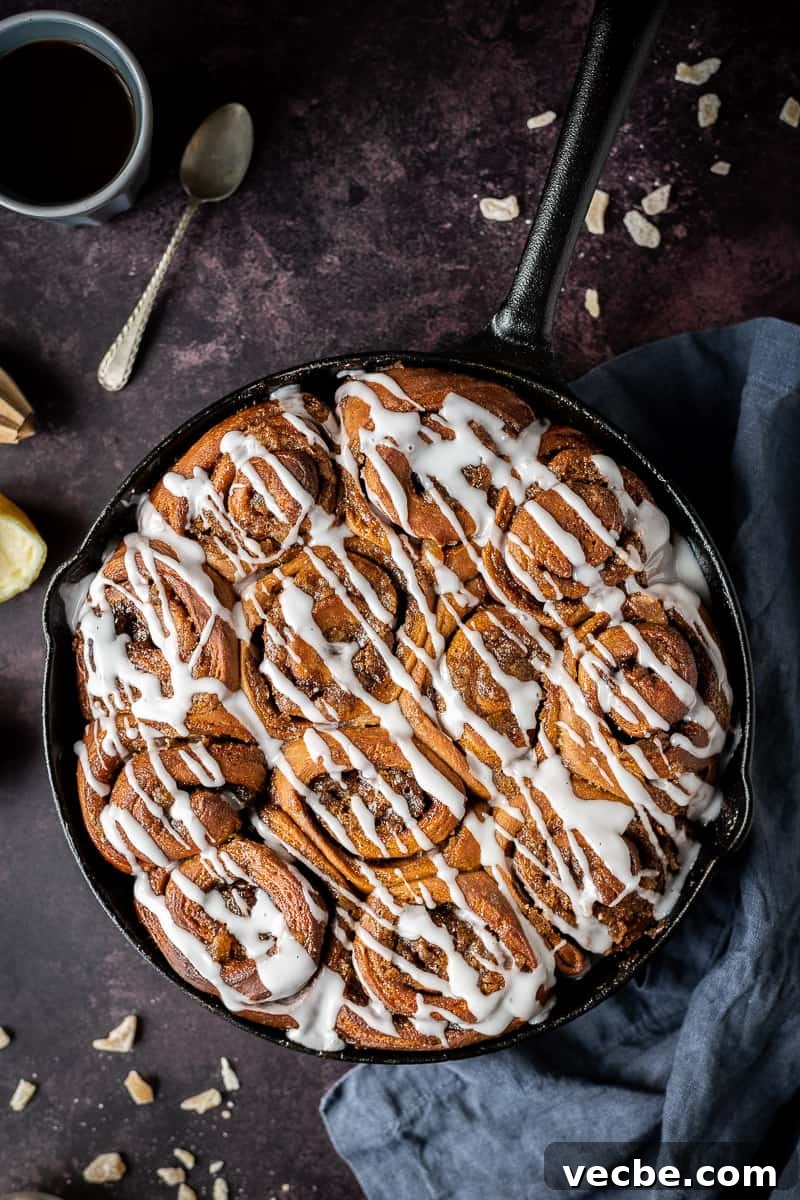 Baked vegan gingerbread cinnamon rolls topped with ginger glaze Baked gingerbread cinnamon rolls in a cast iron skillet on a dark background topped with ginger drizzle glaze.