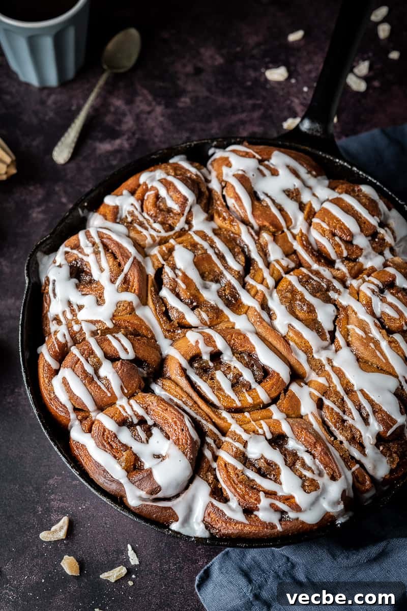 Vegan gingerbread cinnamon rolls served with espresso A skillet of ginger cinnamon rolls on a dark background with chopped candied ginger, a grey cup of espresso and a teaspoon.