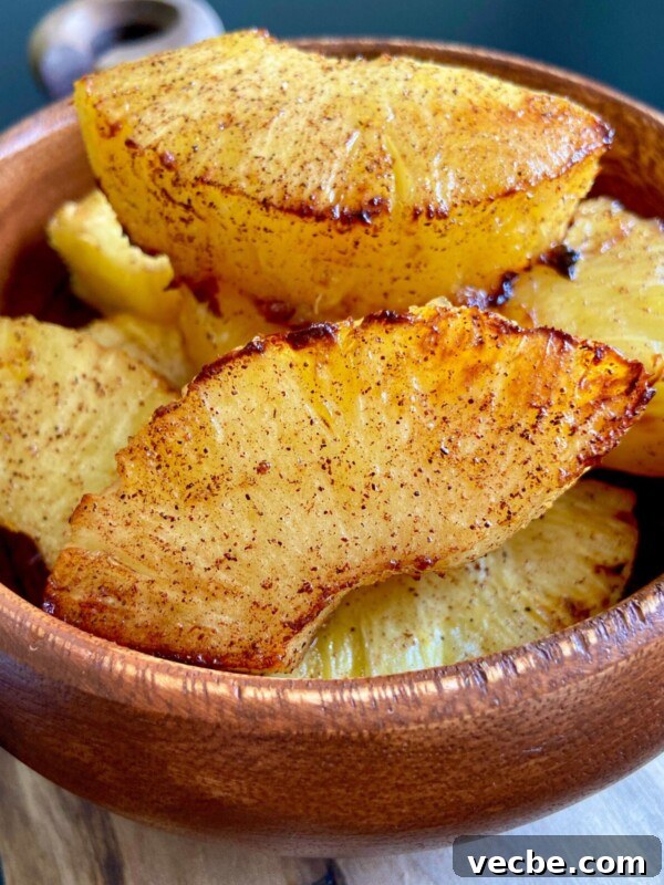 Caramelized Air Fryer Pineapple Recipe 7 A wooden bowl filled with golden brown pineapple slices dusted with cinnamon.