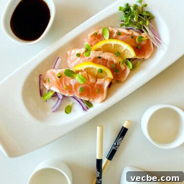 salmon tataki on plate garnished with lemon onion and sprouts next to chopsticks and ponzu