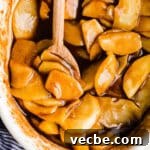 Gluten-Free Apple Recipes: 10+ Desserts, Snacks and More 16 Syrupy cinnamon apples in a white baking dish with a wooden spoon.