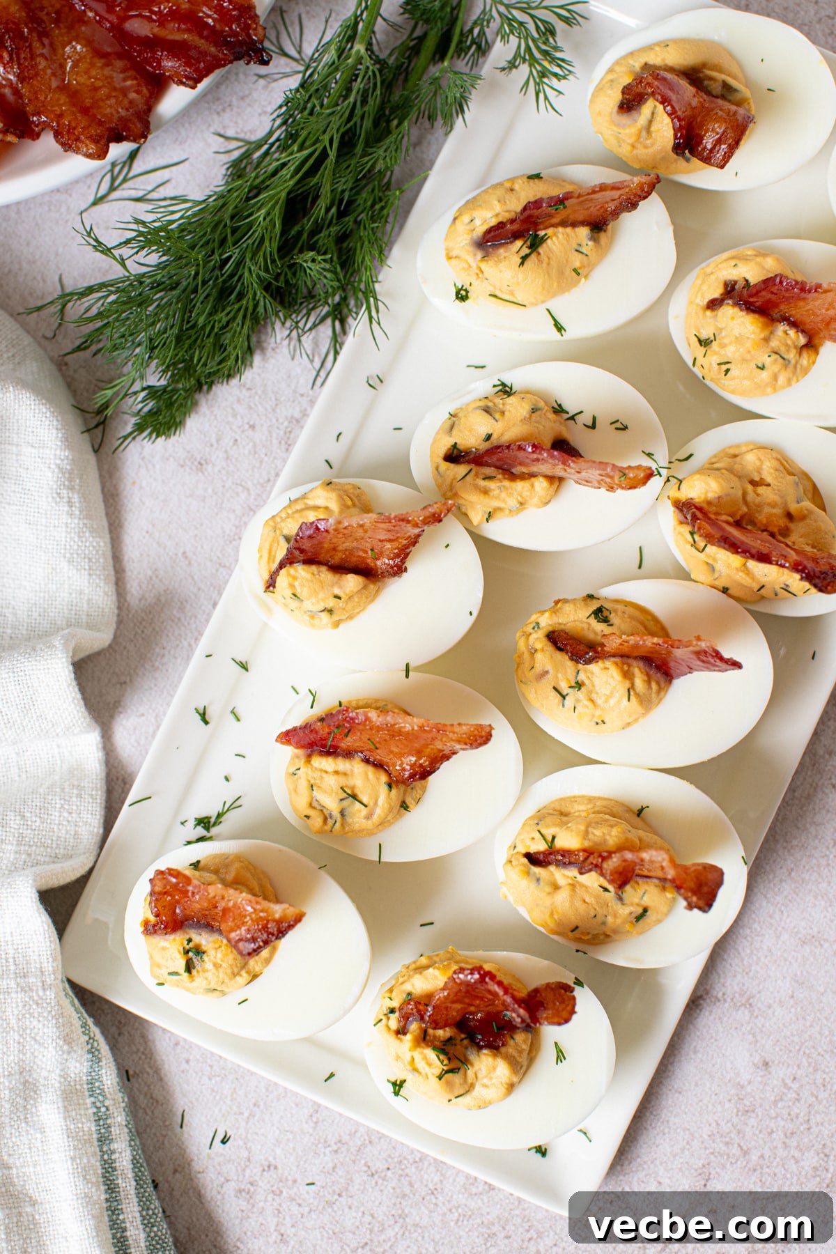 Crispy Candied Bacon Deviled Eggs 4 One dozen deviled eggs with candied bacon sits on a white platter on a white countertop for serving.