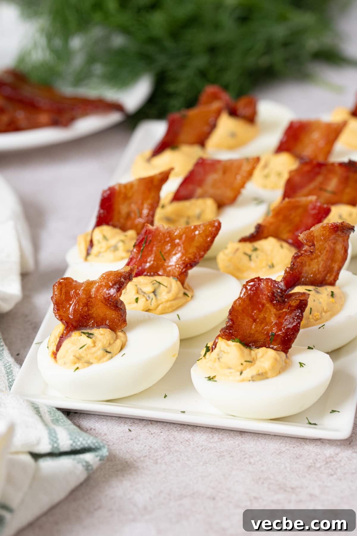 Crispy Candied Bacon Deviled Eggs 5 12 deviled eggs with candied bacon sit on a white serving tray on a countertop.