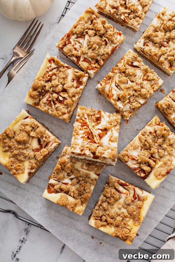 Pumpkin Cheesecake Bars with Creamy Swirl 3 Pumpkin cheesecake bar squares on parchment paper on a cooling rack.