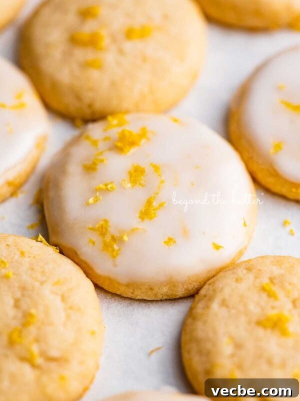 Lemon Meringue Ice Cream Pie Recipe 8 Lemon iced and plain lemon shortbread cookies garnished with lemon zest on white parchment paper.