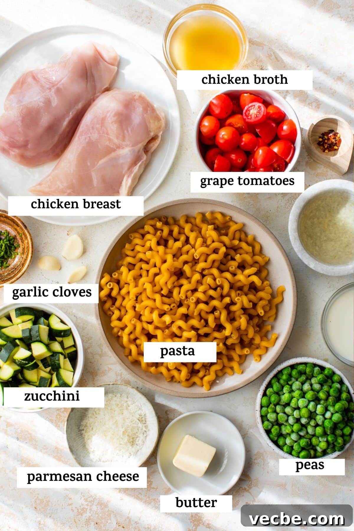 Chicken Pasta Primavera with Fresh Spring Vegetables 3 all ingredients listed on a table; chicken broth, chicken breast, grape tomatoes, garlic cloves, pasta, zucchini, parmesan cheese, butter, and peas