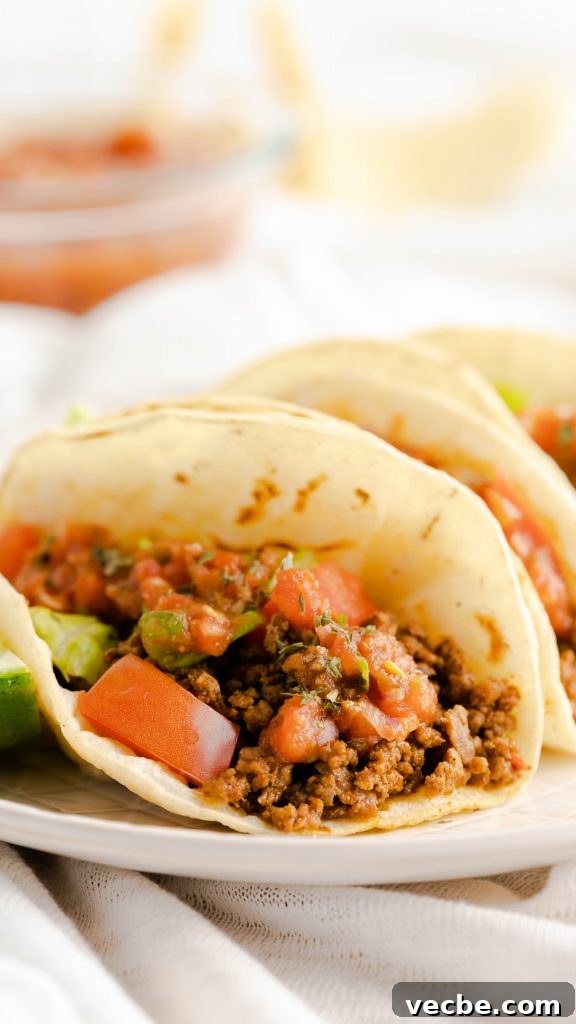 Restaurant-Style Ground Beef Tacos Recipe 3 Close up of ground beef taco with red salsa on a corn tortilla.