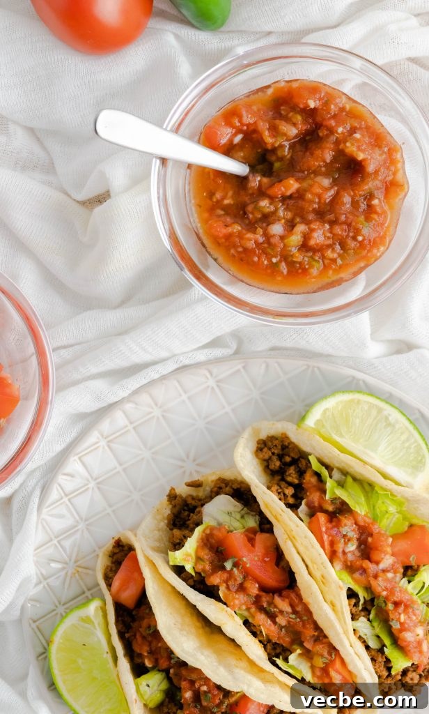 Restaurant-Style Ground Beef Tacos Recipe 5 Top view of three ground beef tacos with sliced limes and a side of red salsa.