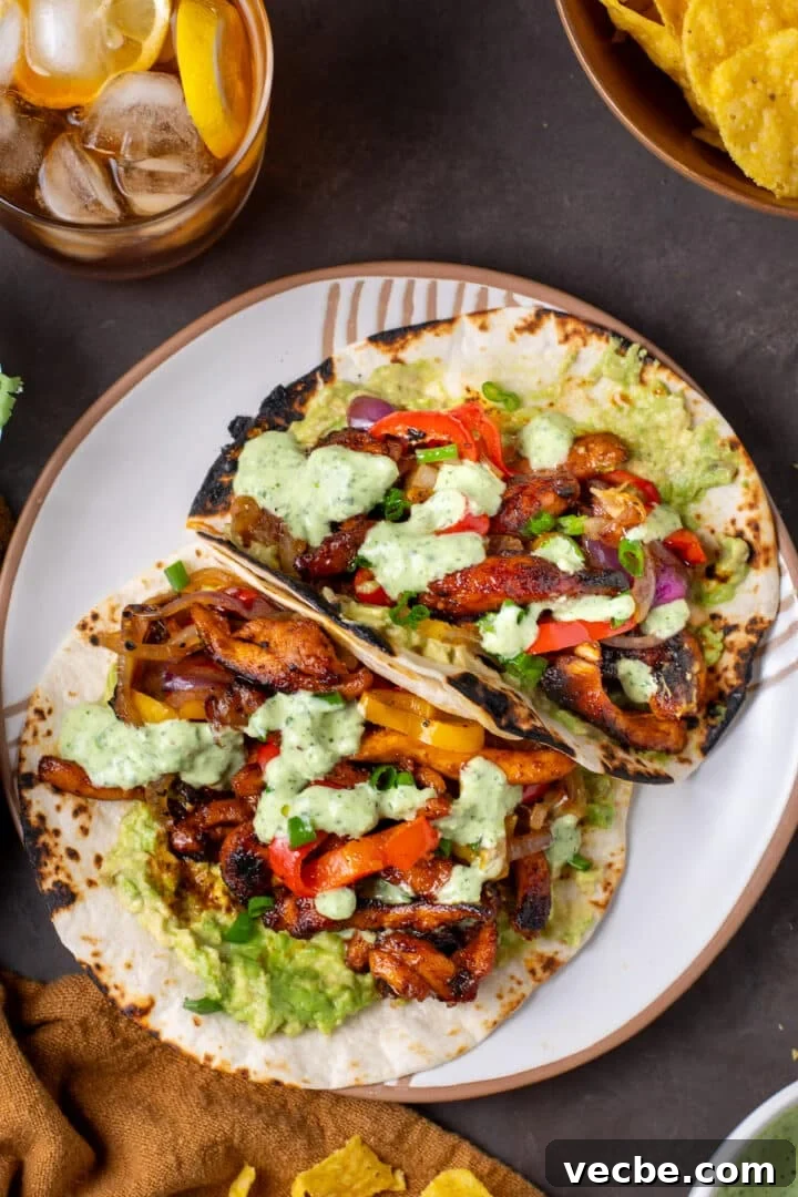 Caramelized Chipotle Chicken Fajitas Recipe 2 white plate with two fajitas filled with chipotle chicken, sauteed veggies, guacamole and cilantro lime yogurt sauce