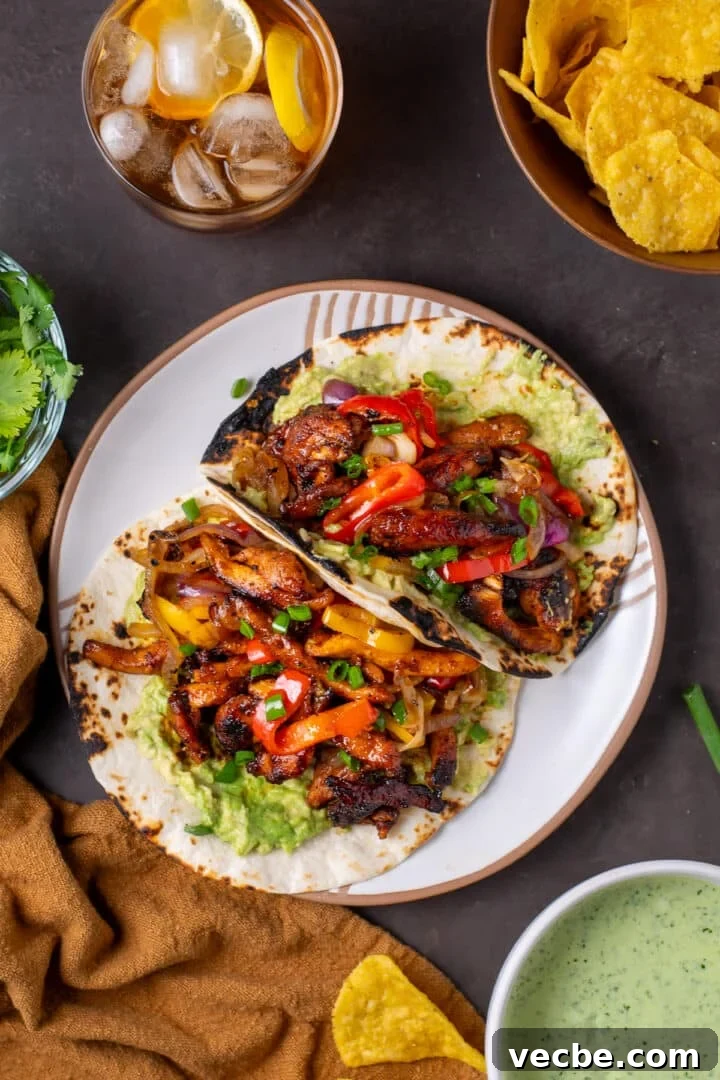 Caramelized Chipotle Chicken Fajitas Recipe 14 white plate with two fajitas filled with chipotle chicken, sauteed veggies, guacamole