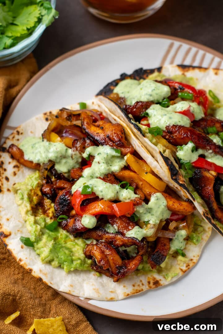 Caramelized Chipotle Chicken Fajitas Recipe 17 white plate with two fajitas filled with chipotle chicken, sauteed veggies, guacamole and cilantro lime yogurt sauce