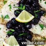 Three pieces of baked mahi mahi sitting on a bed of brown rice topped with blueberry sauce and lemon wedges and sprinkled with chopped parsley.
