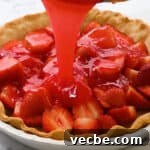 No Bake Strawberry Jello Pie Recipe 11 pouring thickened strawberry jello over halved strawberries in a baked pie crust.