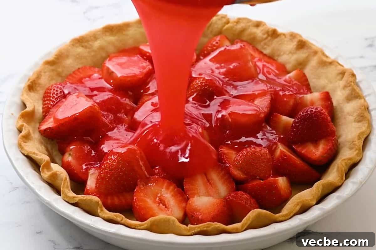 No Bake Strawberry Jello Pie Recipe 18 pouring thickened strawberry jello over halved strawberries in a baked pie crust.