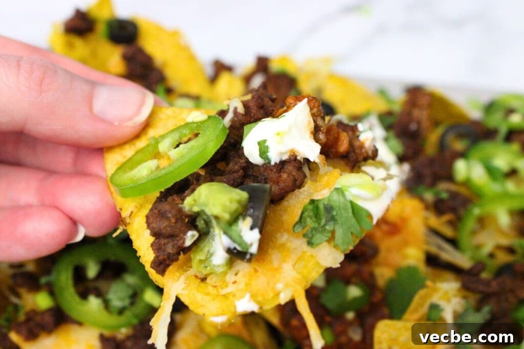 Crispy Air Fryer Ground Beef Nachos for Game Day 3 holding up an air fryer nacho chip with ground beef, jalapeno, sour cream, and black olives
