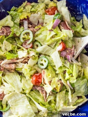 An Italian grinder salad in a large blue bowl topped with cherry tomatoes, chopped banana peppers and parmesan cheese.