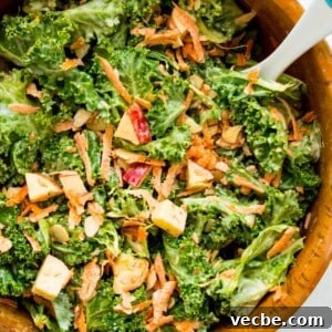 Cabbage-Free Kale Slaw with Apples and Carrots 12 A wooden salad bowl filled with a kale apple salad with a serving spoon in it.