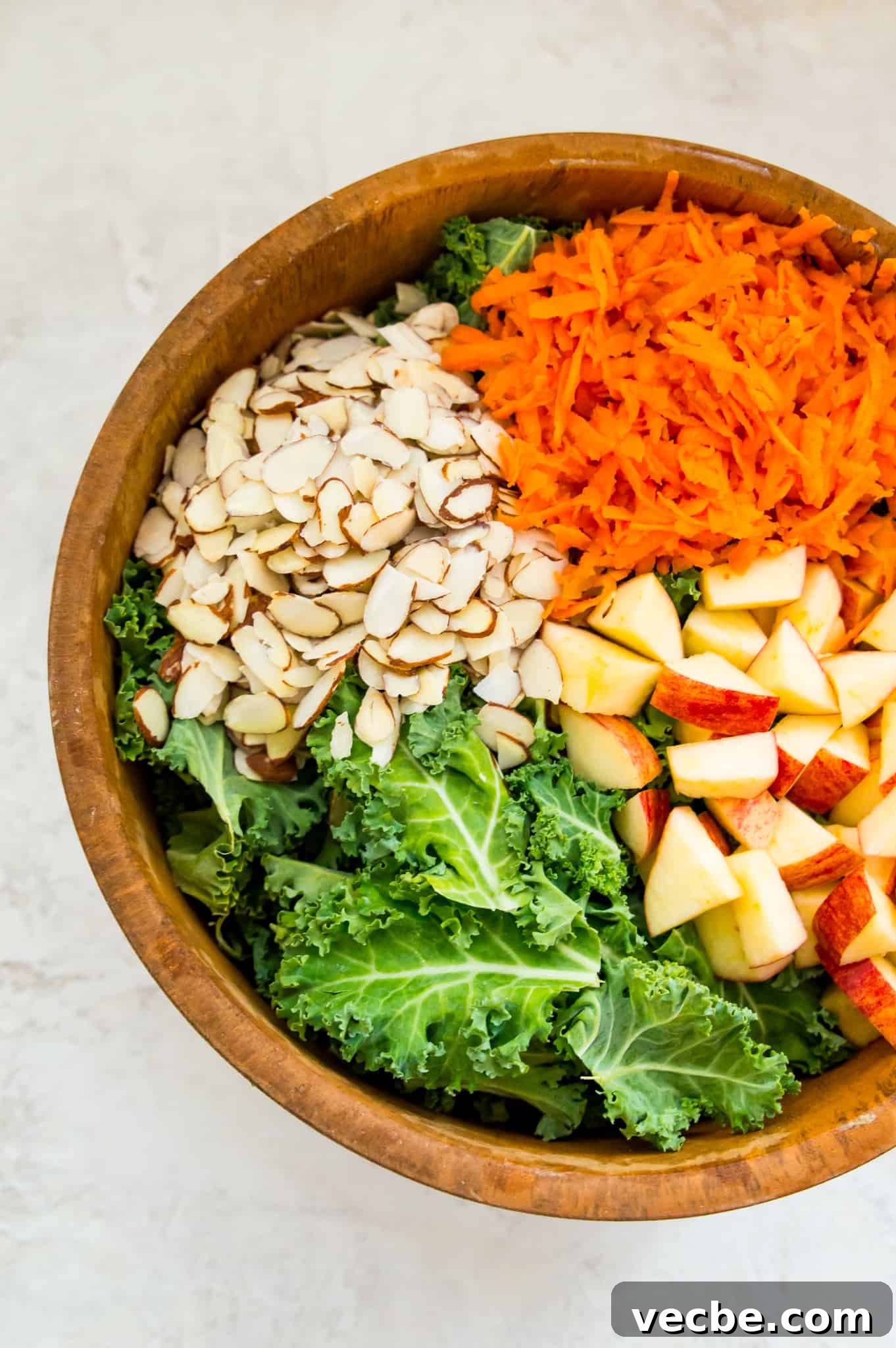 Cabbage-Free Kale Slaw with Apples and Carrots 4 A wooden salad bowl filled with chopped kale, slivered almonds, chopped apples and shredded carrots.