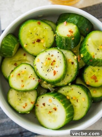 A bowl of Din Tai Fung cucumber salad topped with chili flakes and with a spoon beside it.