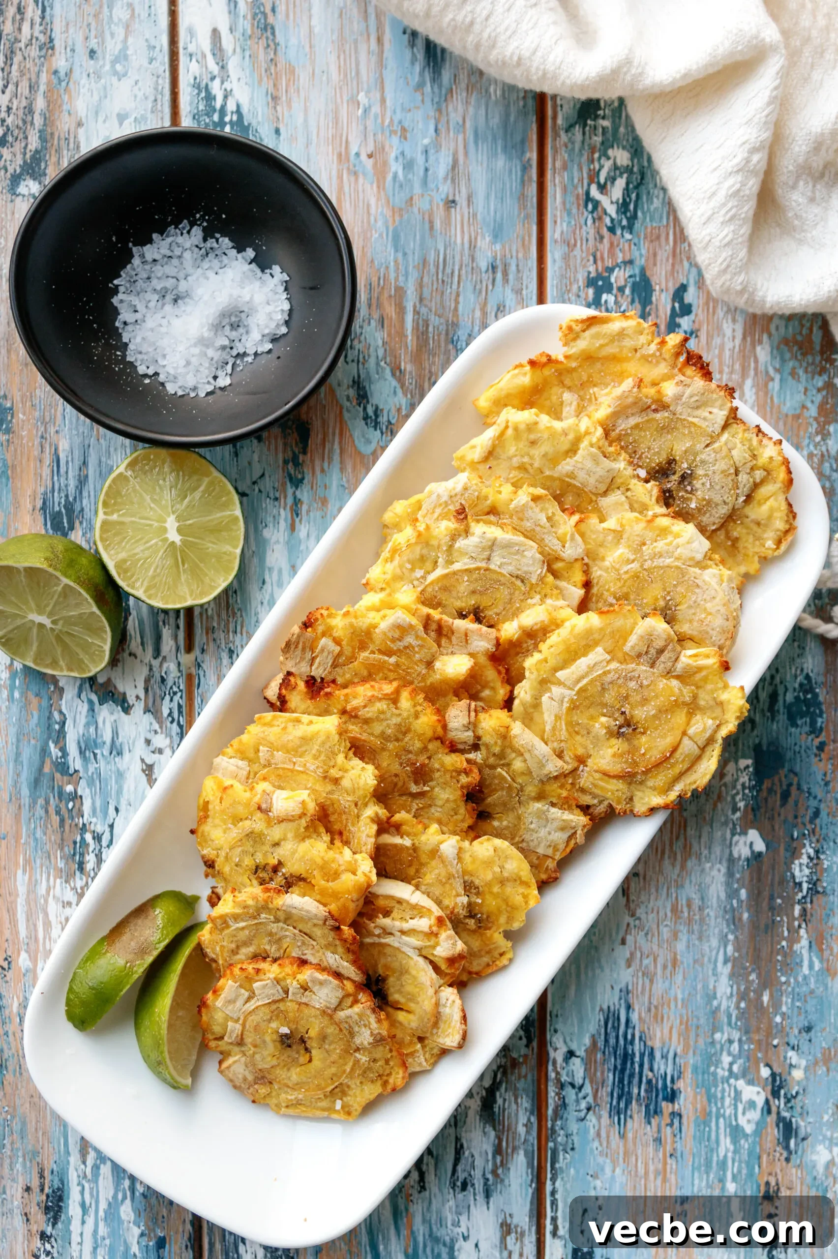 Air Fryer Tostones Cuban Fried Plantains 4 top view of the tostones on a mottled blue background with a dish of salt and cut lime as garnishes