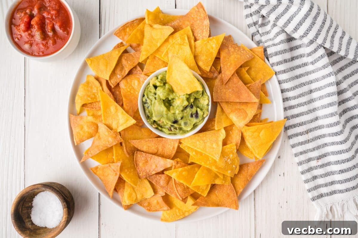 Crispy Baked Corn Tortilla Chips Recipe 2 Top down view of a white platter containing a bowl of guacamole surrounded by homemade baked corn tortilla chips - Hostess At Heart