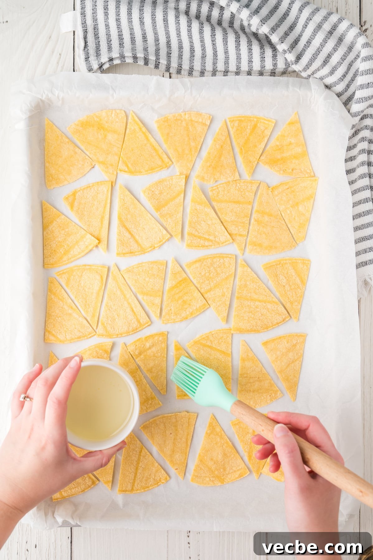 Crispy Baked Corn Tortilla Chips Recipe 5 Top down view of a parchment paper-lined baking sheet filled with cut corn tortillas for making chips - Hostess At Heart