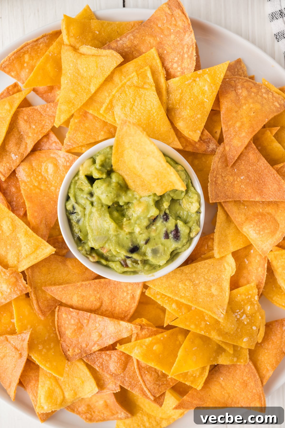 Crispy Baked Corn Tortilla Chips Recipe 9 Closeup view of a platter with a bowl of guacamole surrounded by homemade corn tortilla chips - Hostess At Heart