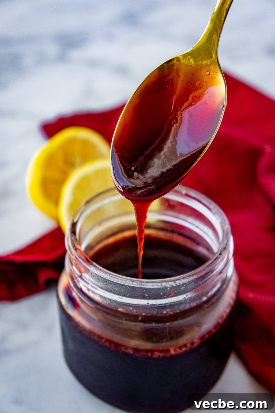 How to Make Pomegranate Molasses from Scratch 2 pomagranate molasses drizzling from a gold spoon into a jar.