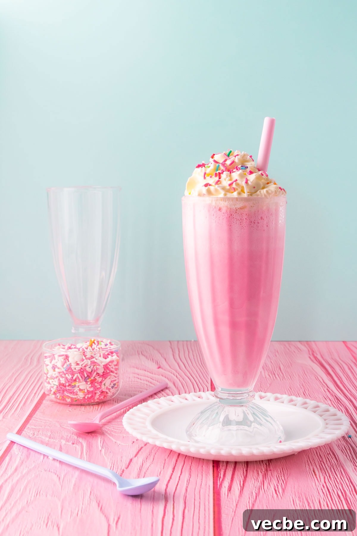 Pink Panther Raspberry Lemonade Ice Cream Float Recipe 2 Two pink panther drinks in tall glasses with striped paper straws on a white table with a yellow and white striped background.