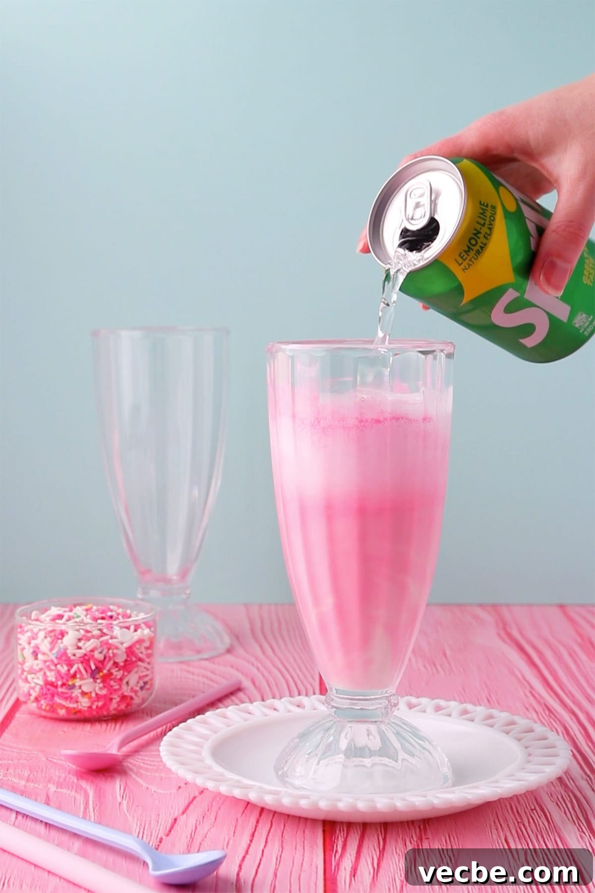 Pink Panther Raspberry Lemonade Ice Cream Float Recipe 5 A hand pouring lemonade from a can into the glass - the pink mixture is frothing up.