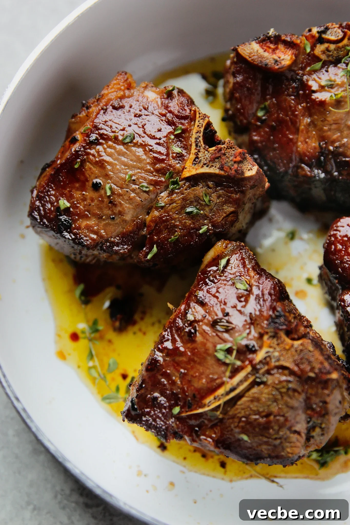Pan-Seared Garlic & Herb Lamb Loin Chops 2 close up on 2 seared lamb loin chops in a white pan.