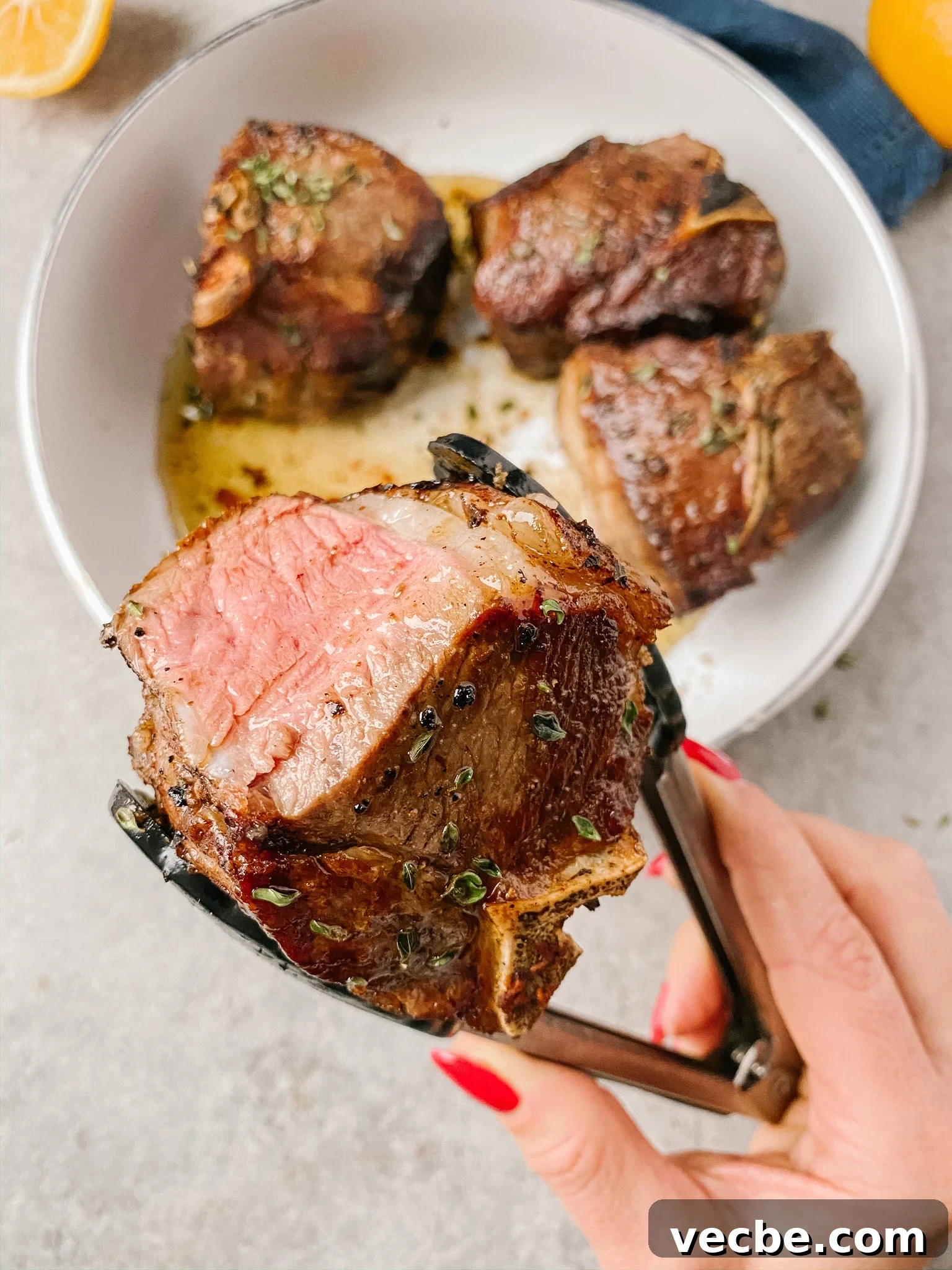 Pan-Seared Garlic & Herb Lamb Loin Chops 7 hand holding a cooked lamb loin chop with kitchen tongs.