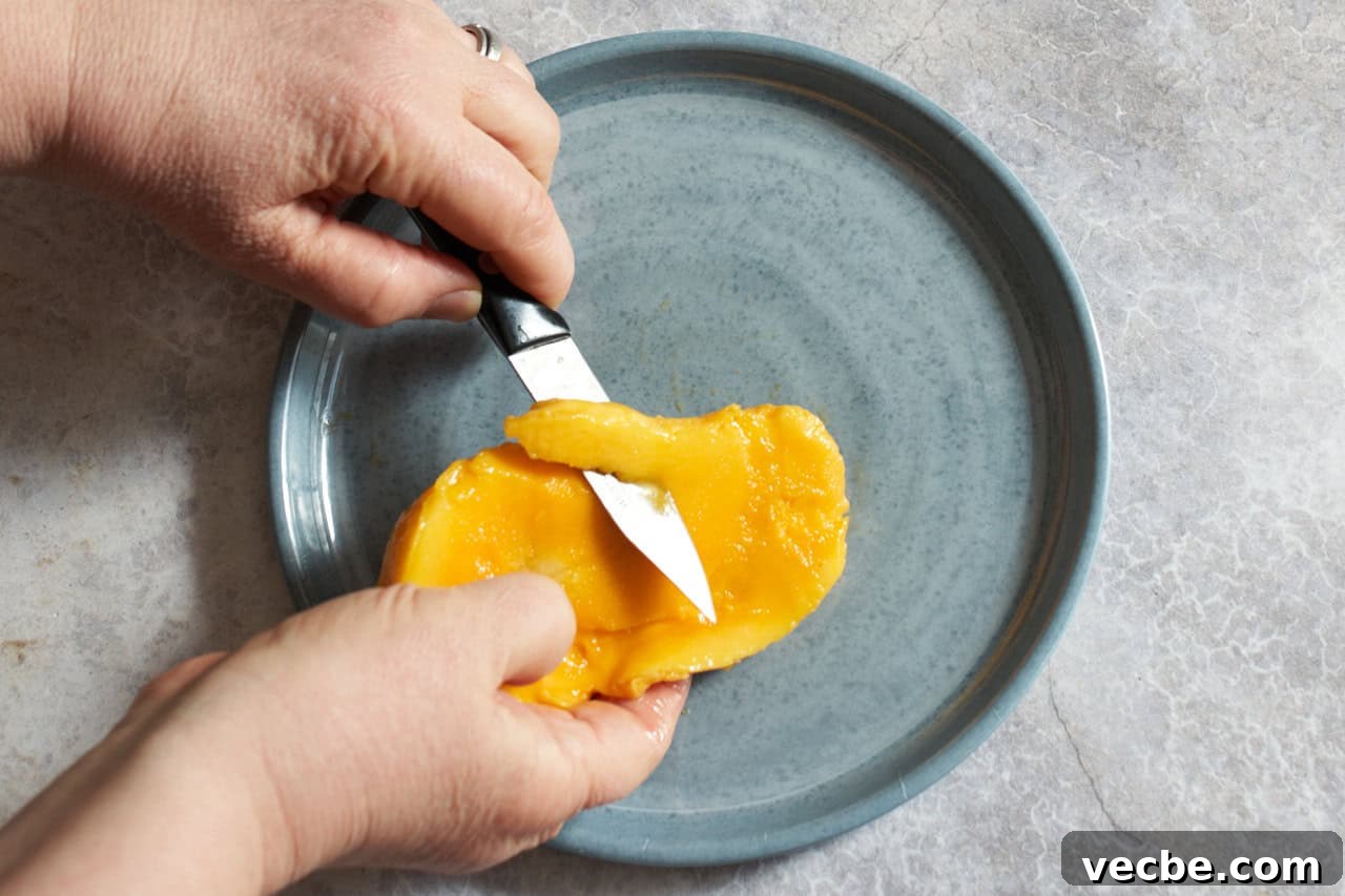 How to Cut a Mango Like a Pro 5 A woman's hands are shown using a paring knife to cut strips of fruit away from a mango seed.