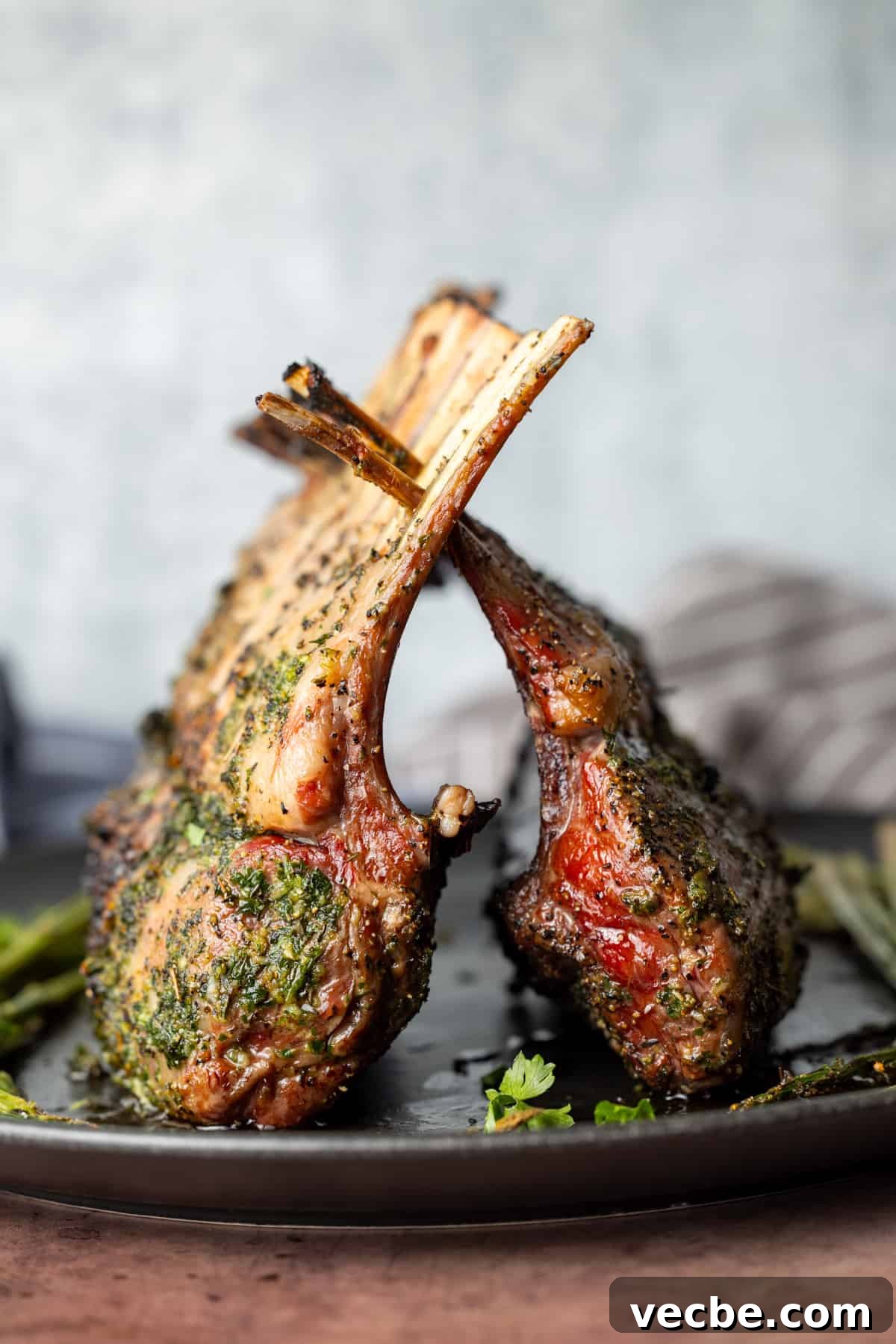 Smoked Lamb Chops Recipe with Garlic and Rosemary 2 Two racks of lamb cooked on top of a black plate with white background.