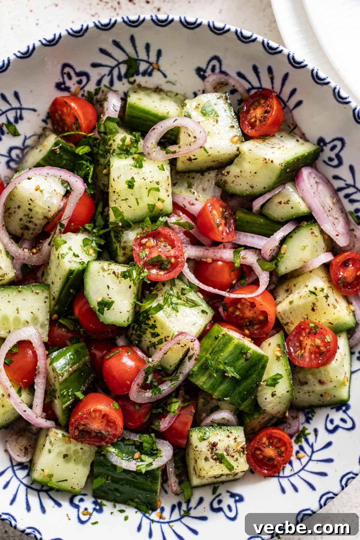 Refreshing Mediterranean Cucumber Salad with Feta and Mint 5 A blue and white patterned bowl filled with cucumber and tomato salad with mediterranean spices on top.