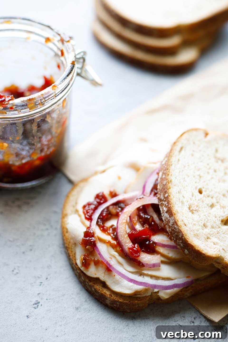 Homemade Sweet and Spicy Pepper Relish Recipe 3 Turkey sandwich topped with red onion slices and hot pepper relish, with a nearly empty jar of relish in background.