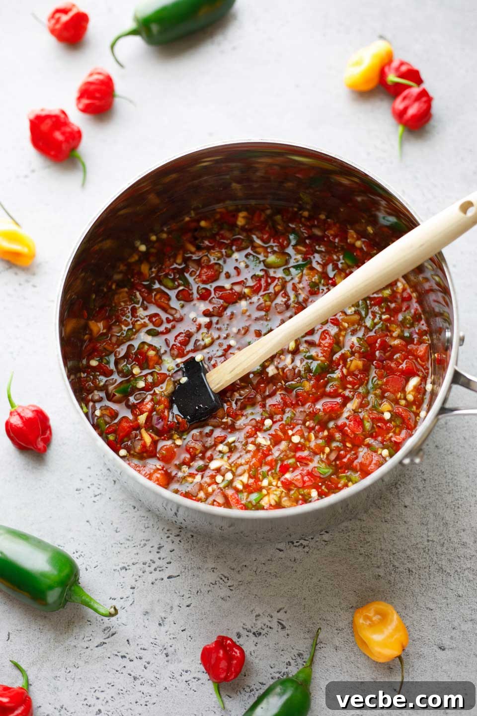Homemade Sweet and Spicy Pepper Relish Recipe 7 Large silver pot full of ingredients being stirred, with raw hot peppers scattered in background.
