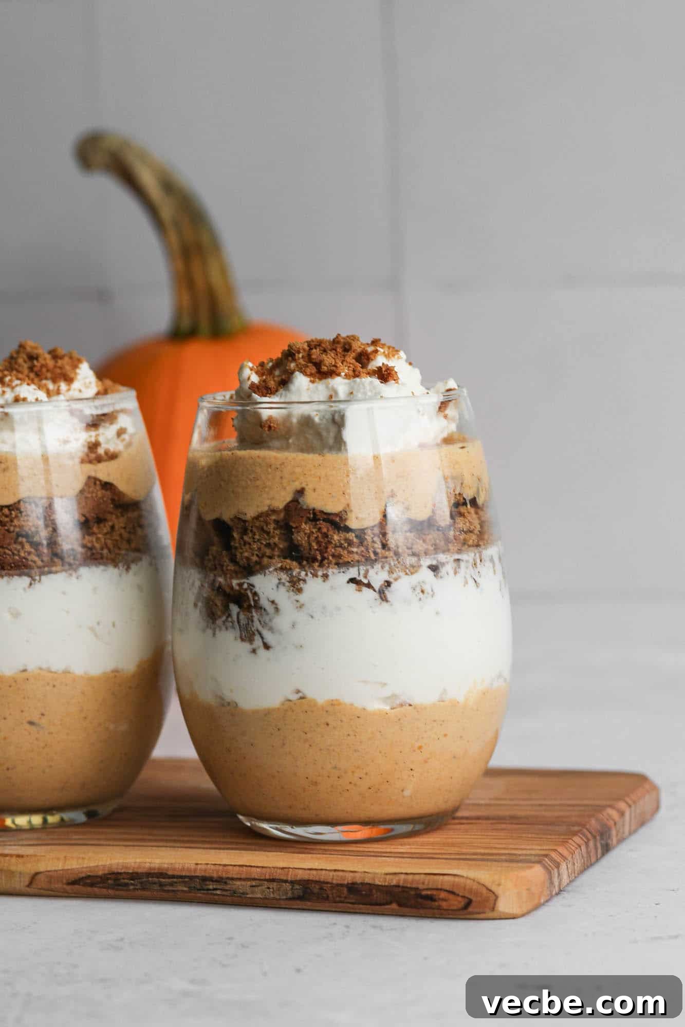Irresistible Gluten-Free Fall Dessert Recipes 2 a stemless wine glass with layers of pumpkin mousse, whipped cream and gluten free gingersnap cookies with an orange pumpkin sitting behind it