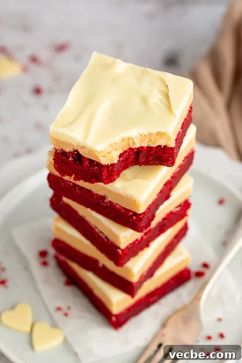 Red Velvet Millionaire Brownies Recipe with Caramel and Chocolate 3 A stack of 5 red velvet millionaire brownies set on two stacked plates with a fork on the side. The top one has a bite taken out of it.