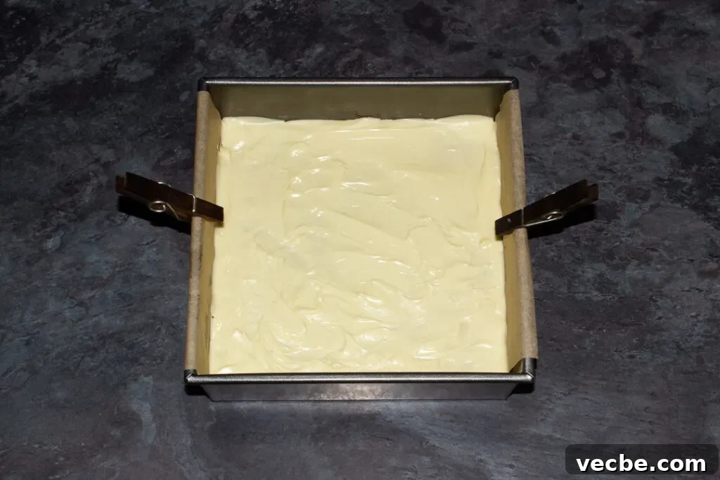 Red Velvet Millionaire Brownies Recipe with Caramel and Chocolate 13 A lined square baking tin with melted white chocolate poured over caramel and red velvet brownie.