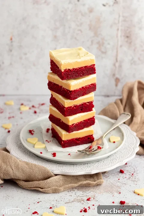 Red Velvet Millionaire Brownies Recipe with Caramel and Chocolate 14 A stack of 5 red velvet millionaire brownies set on two stacked plates with a fork on the side.