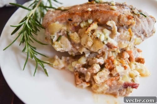Apple, Bacon and Blue Cheese Stuffed Pork Chops Recipe 3 apple bacon blue cheese stuffed pork chop on white plate with sprig of rosemary close up view
