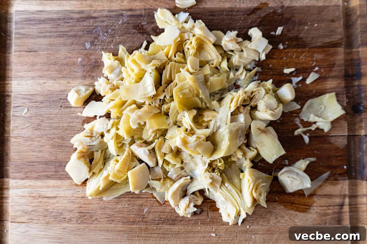 Creamy Hot Artichoke Dip Recipe 5 Chopped artichoke hearts on a wooden cutting board.
