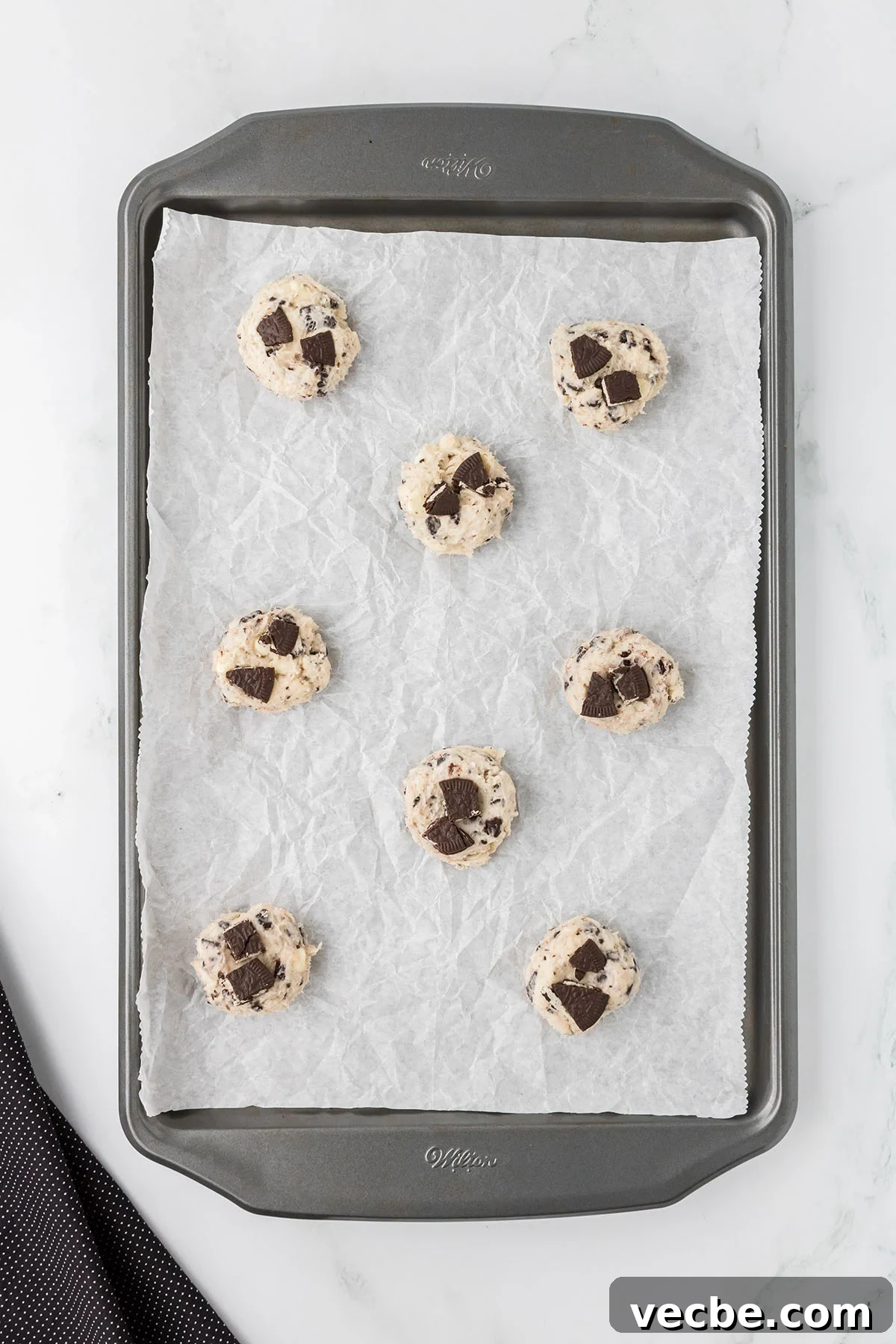 Cookies and Cream Cheesecake Cookie Bites 8 Crushed Oreos are placed on top of the cookie dough balls on the baking sheet.