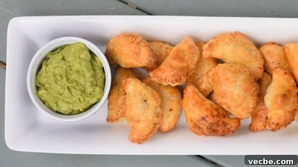 19 Budget-Friendly Meals to Replace Takeout 2 Image shows an overhead shot of Puff Pastry Beef Empanadas on a white tray with a bowl of guacamole to the left of them.