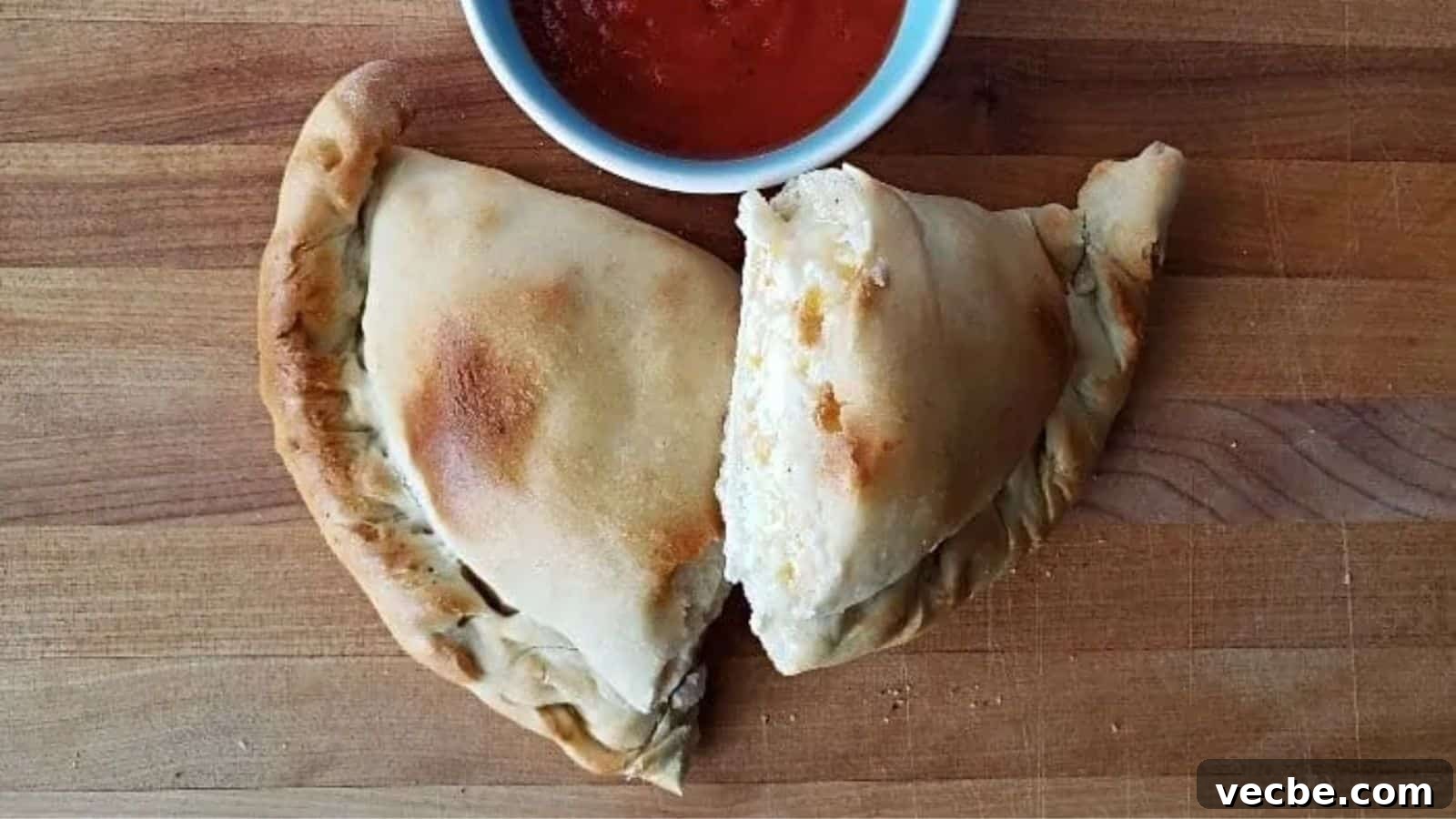19 Budget-Friendly Meals to Replace Takeout 17 Image shows an overhead shot of a Calzone cut in half on a wooden board with a small bowl of marinara above it.