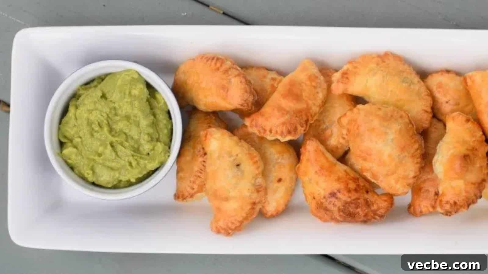 19 Budget-Friendly Meals to Replace Takeout 8 Image shows an overhead shot of Puff Pastry Beef Empanadas on a white tray with a bowl of guacamole to the left of them.