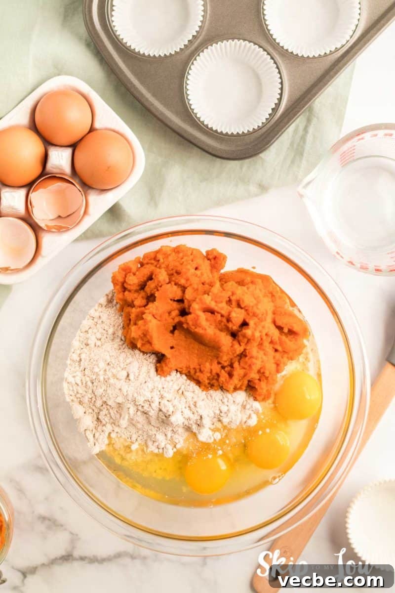Pumpkin Cake Mix Muffins Recipe 4 cake mix, pumpkin, eggs and water in a large bowl; there is also a carton of eggs with cracked and whole brown eggs, muffin pan with paper cups adn liquid measuring cup